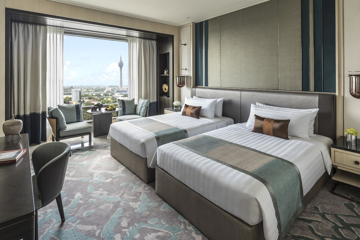 Une chambre d’hôtel avec deux lits, un bureau, une chaise et une vue sur le paysage urbain.