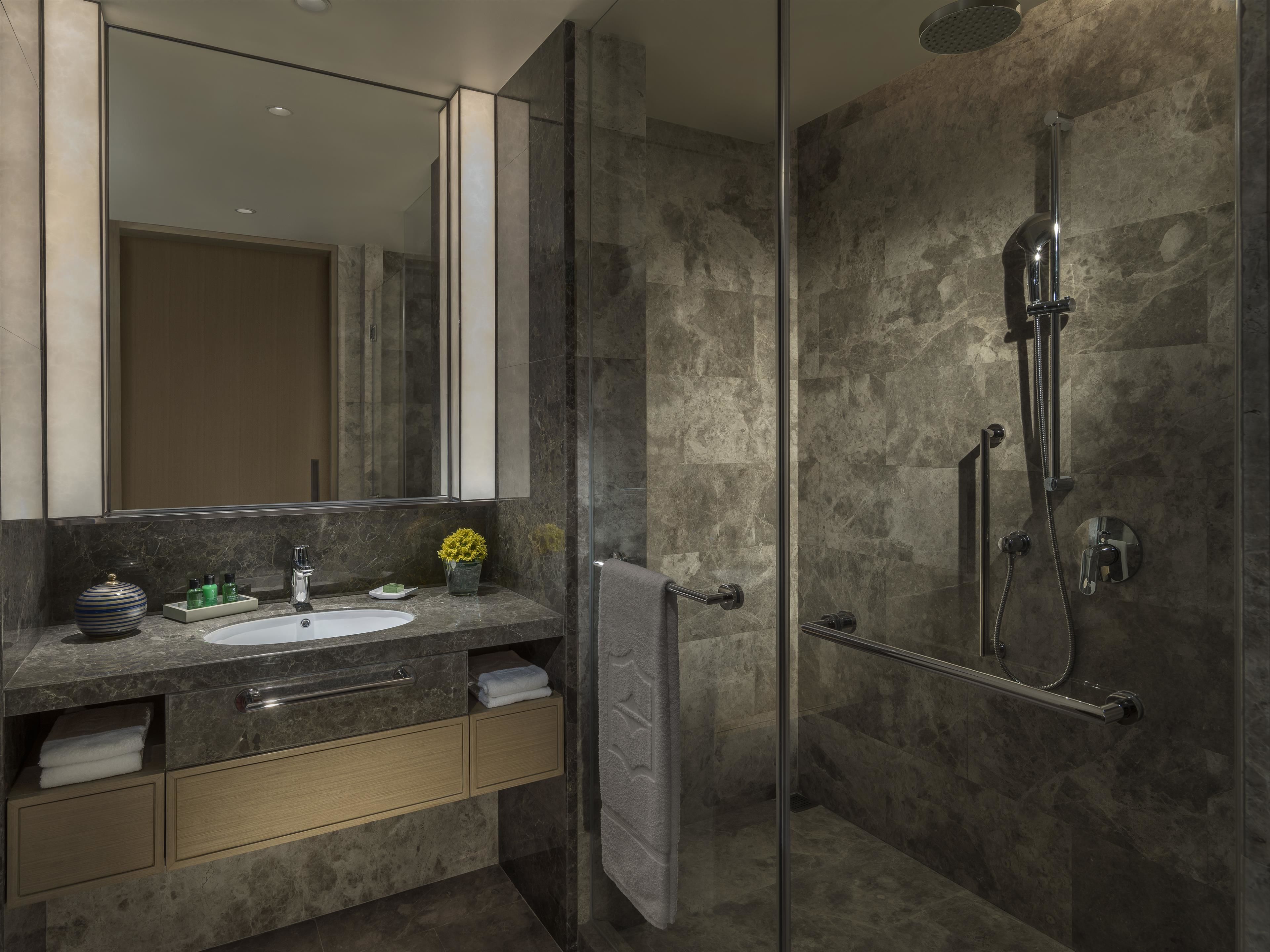 A modern bathroom with a glass shower enclosure, a marble sink, and a large mirror.