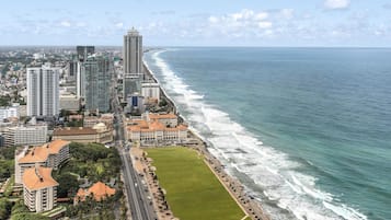 Paisagem costeira com edifícios altos, calçadão à beira-mar e uma grande área de parque verde.