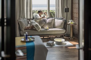 A person in a robe sitting on a striped sofa with a table beside them containing a teapot, cups, and a bowl of fruit. - Shangri-La Colombo (Colombo)