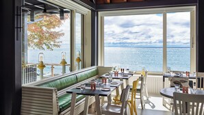 Un restaurante con vista al mar, que cuenta con un banco acolchado verde, sillas blancas y mesas dispuestas con vasos y cubertería.