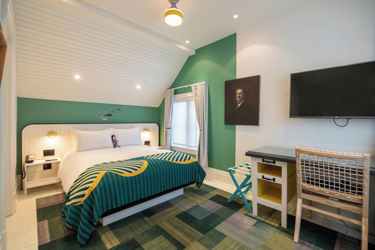 A hotel room with a bed, a desk, a chair, a TV, and a window with curtains.