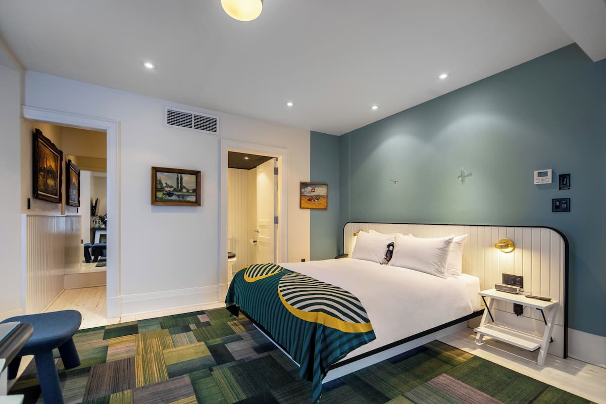 A bedroom with a bed, bedside table, nightstand, and a chair.
