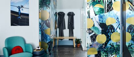 A modern room with a teal armchair, a bench, and a glass partition with abstract art.