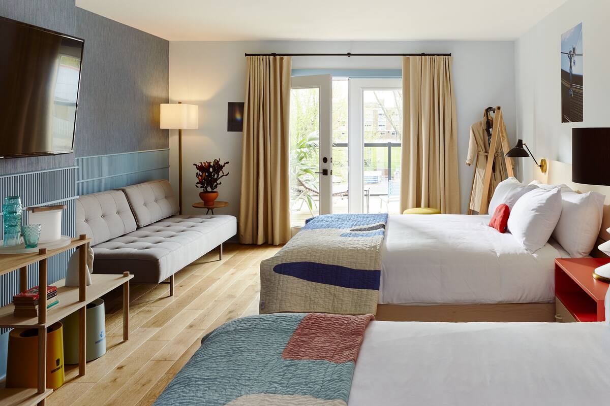 A hotel room with two beds, a sofa, a TV, and a balcony with curtains.