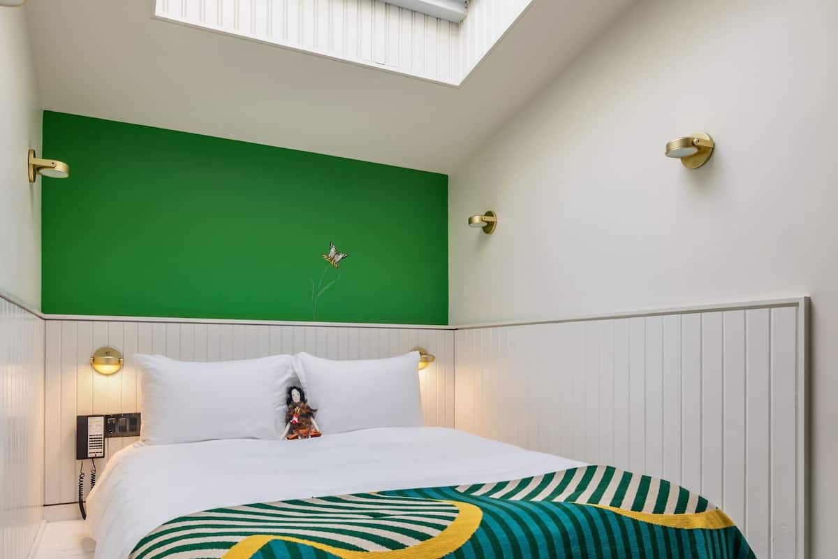 A hotel room with a skylight, a green accent wall, a bed with white bedding, and a decorative pillow.