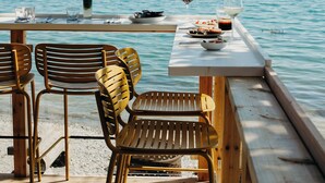 Terraza de madera con una mesa dispuesta para dos, con vista al mar tranquilo.