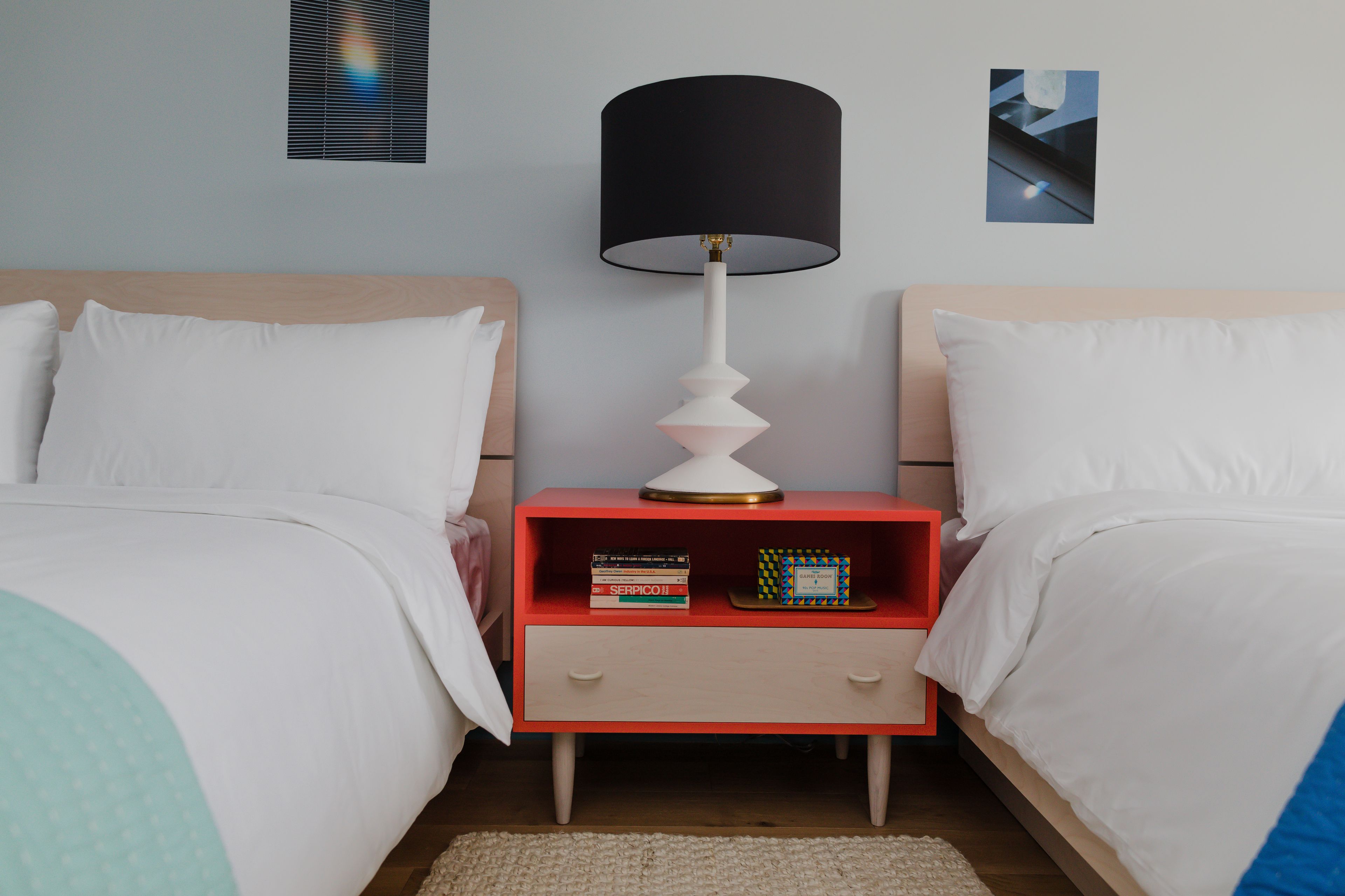 Una camera da letto con due letti, un comodino con una lampada e una piccola mensola con libri e una sveglia.