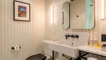 Une salle de bain avec des toilettes, un lavabo et deux miroirs. Un tableau encadré est accroché au mur, et il y a un porte-serviettes avec des serviettes.