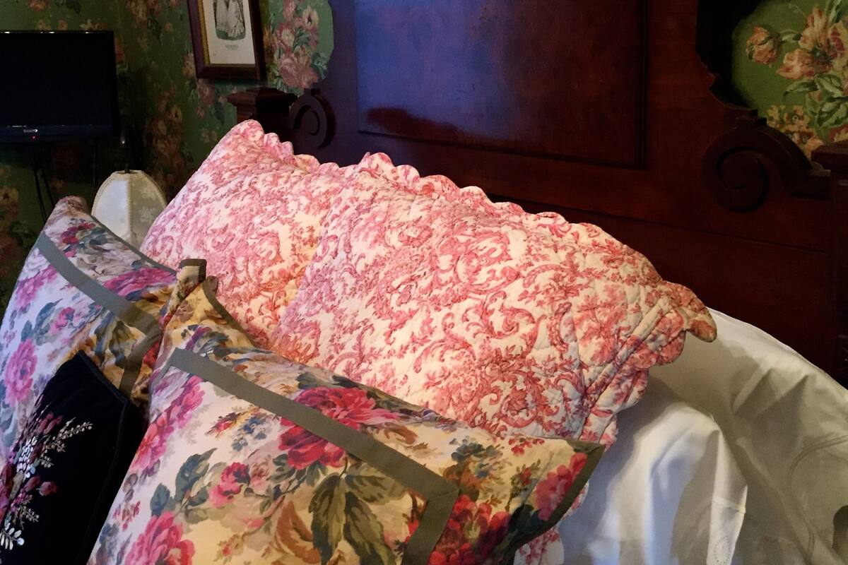 A bedroom with a floral-patterned bedspread, a wooden headboard, and a green floral wallpaper.