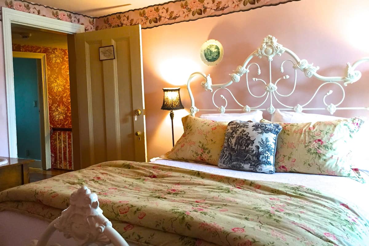 A bedroom with a floral-patterned bedspread, a white ornate headboard, and a bedside lamp.
