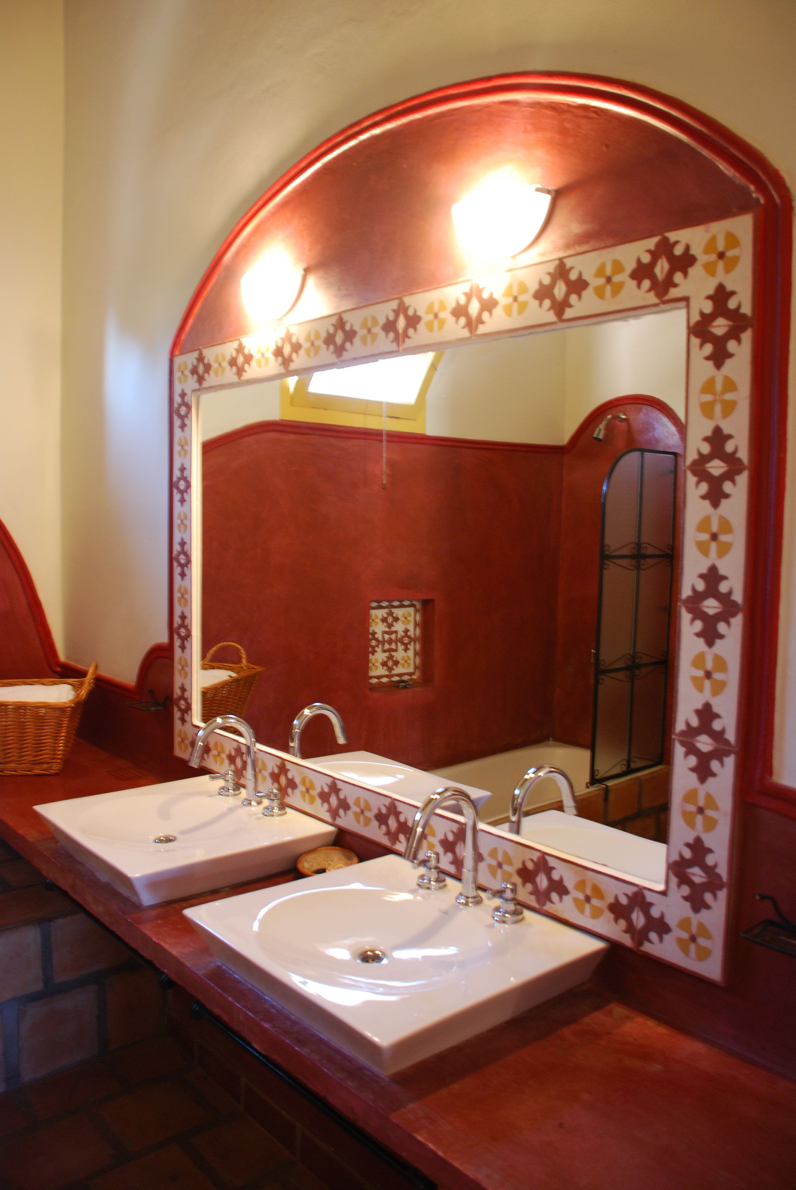 Un baño con dos lavamanos, un espejo grande y una pared roja.