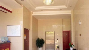 Un hall d’entrée spacieux avec un comptoir d’accueil, une plante en pot, une table en verre et un ascenseur moderne.