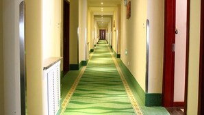 Un couloir d’hôtel avec un tapis vert, des murs de couleur crème et des portes rouges.