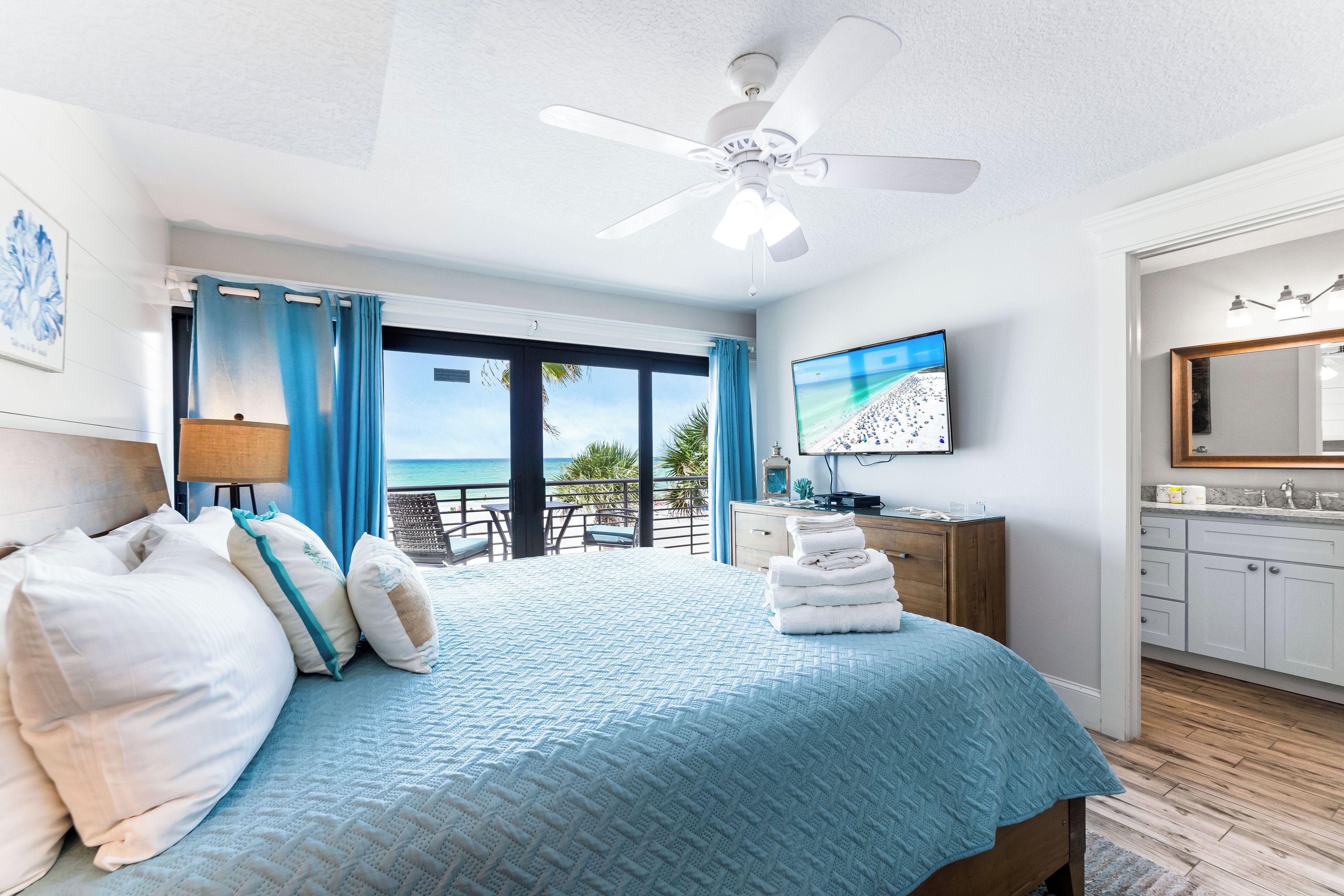 A bedroom with a bed, a ceiling fan, a TV, and a view of the ocean.