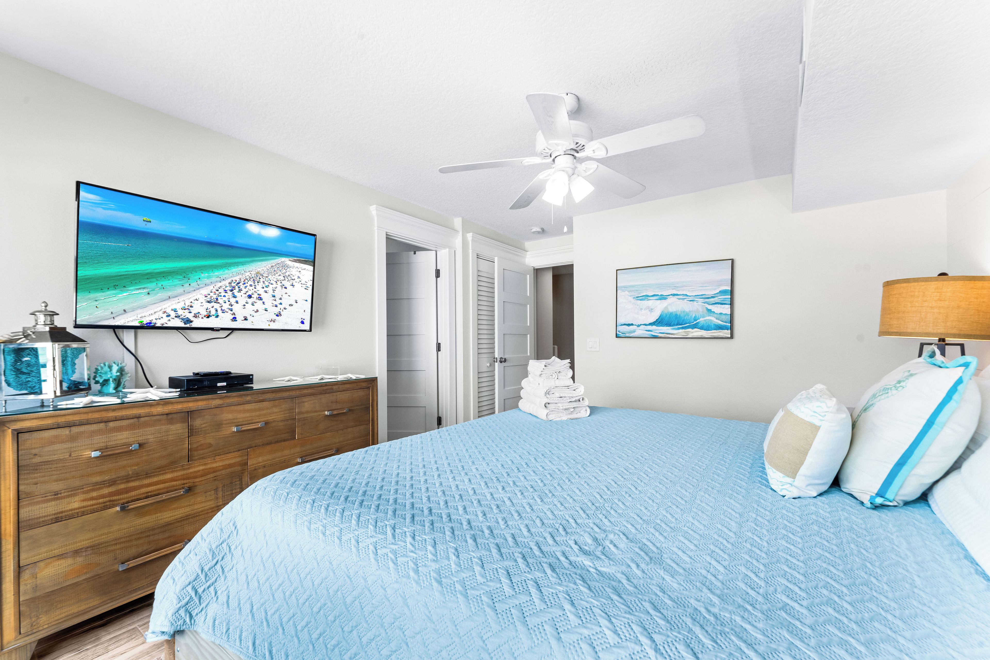 Ein Schlafzimmer mit Bett, Fernseher, Deckenventilator und einer Tür zu einem Badezimmer.