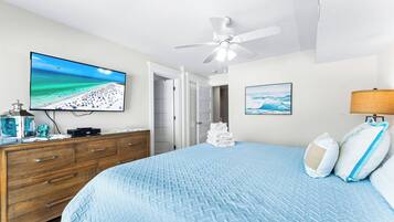 Ein Schlafzimmer mit Bett, Fernseher, Deckenventilator und einer Tür zu einem Badezimmer.