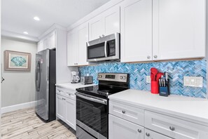 A modern kitchen with white cabinets, stainless steel appliances, a microwave, a toaster, and a red utensil holder. - Fanta-Sea on the Beach by Beachside Management - 49 Beach Rd (Siesta Key)