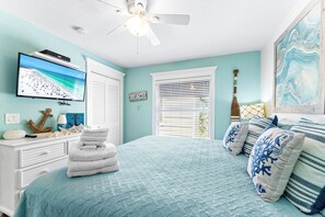 A bedroom with a bed, a television, a ceiling fan, and a window with blinds. - Fanta-Sea on the Beach by Beachside Management - 49 Beach Rd (Siesta Key)