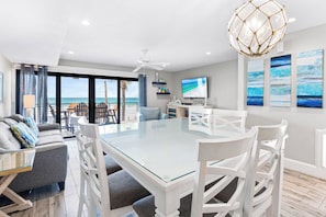 A modern dining area with a glass table and white chairs, overlooking a beach. - Fanta-Sea on the Beach by Beachside Management - 49 Beach Rd (Siesta Key)