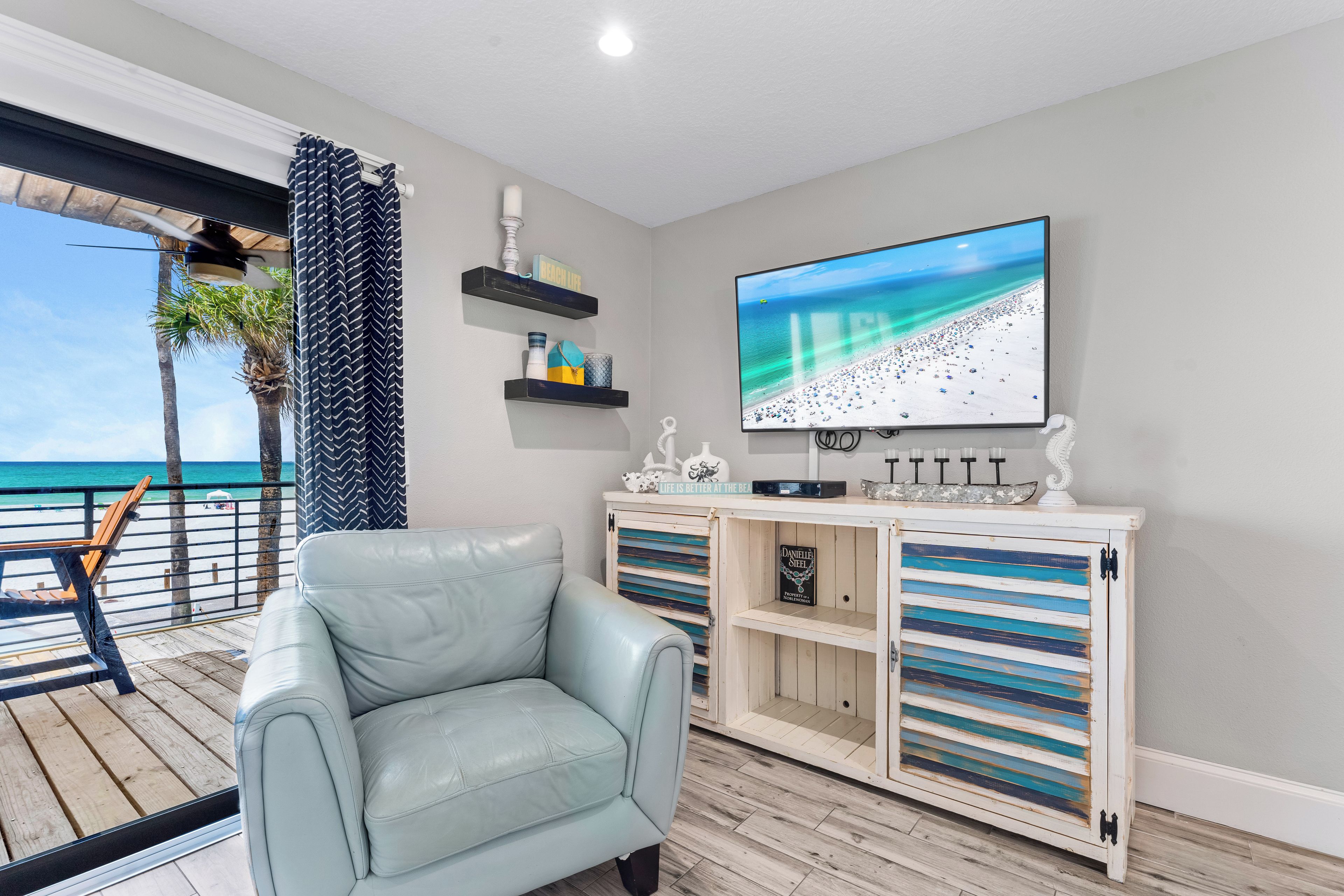 A modern living room with a leather sofa, a flat-screen TV, and a view of the beach.