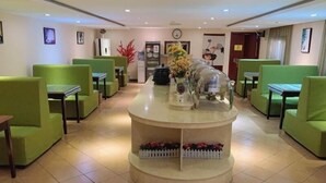 A hotel lobby with green seating, a central counter with a flower arrangement, and a clock on the wall.