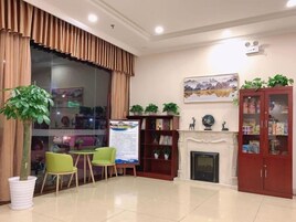 Un salón luminoso con chimenea, una estantería, un sofá verde y un ventanal con cortinas.