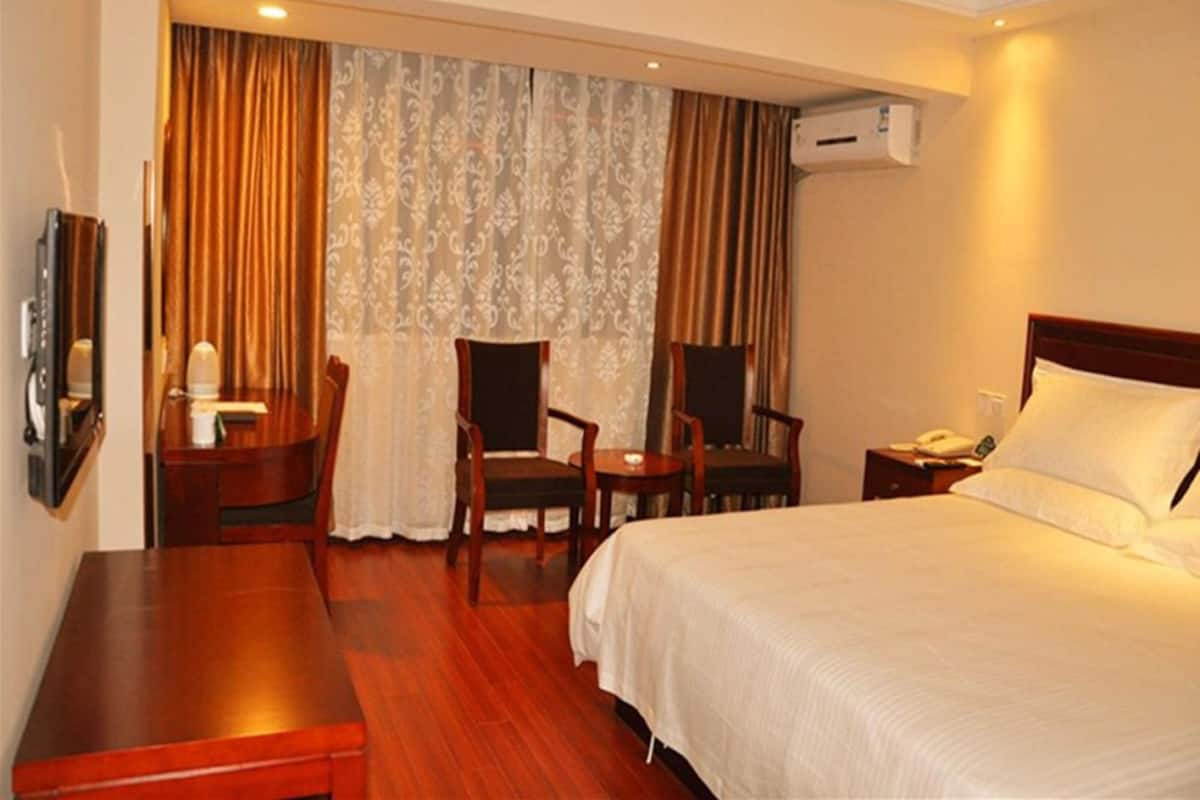 A hotel room with a bed, a desk, two chairs, a TV, and an air conditioning unit.