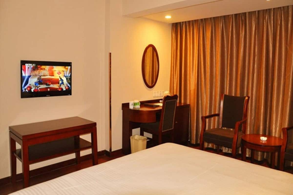 A hotel room with a bed, a desk, a chair, a television, and a curtain.