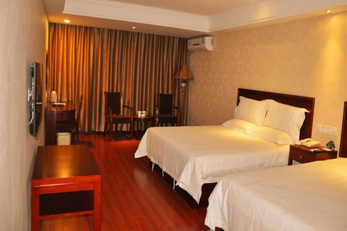 A hotel room with two beds, a desk, a chair, a TV, and an air conditioning unit.