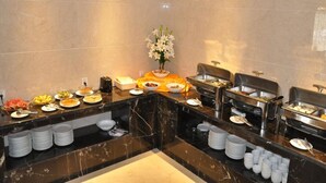 A buffet setup with various food items and serving utensils, arranged on a marble countertop with a vase of flowers in the center. - GreenTree Inn Taizhou Taixing East Guoqing Road RT Mart Business Hotel (Taizhou)
