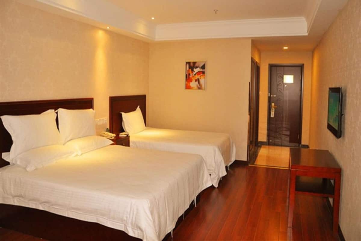 A hotel room with two beds, wooden flooring, a painting on the wall, and a door leading to another room.