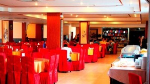 Restaurante com cadeiras e mesas vermelhas, área de bar e piso ladrilhado.