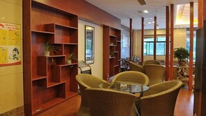 Um hall com estantes de madeira, cadeiras de vime e uma mesa de vidro.