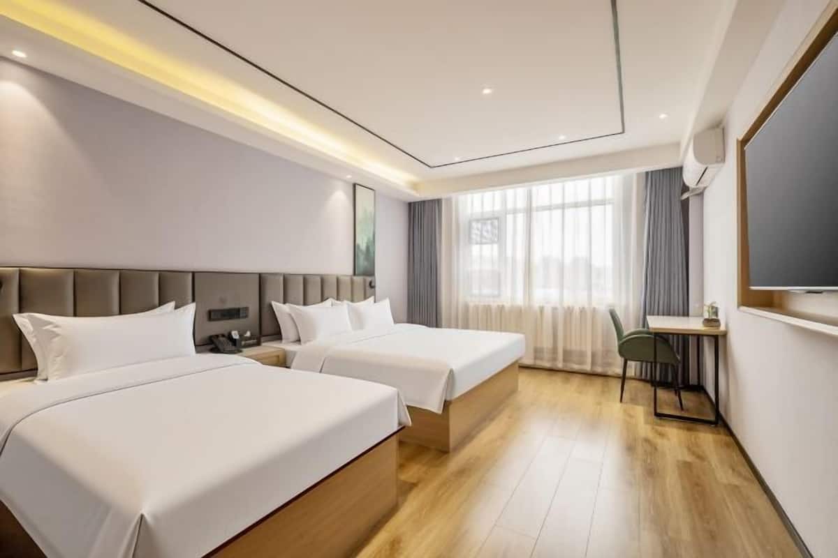 A hotel room with two beds, a desk, and a large window.