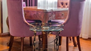 Une table à manger avec un plateau en verre et un pied en métal, entourée de chaises recouvertes d’un tissu violet.