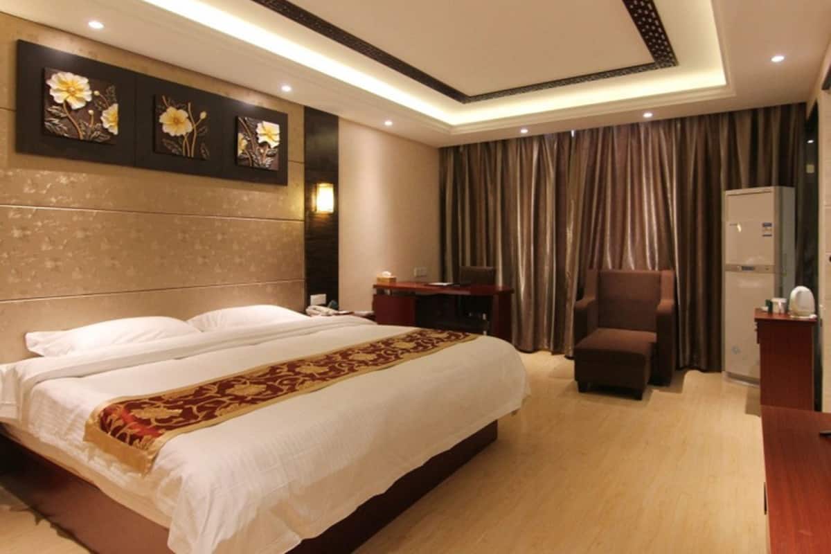 A hotel room with a large bed, a desk, a chair, and a minibar.
