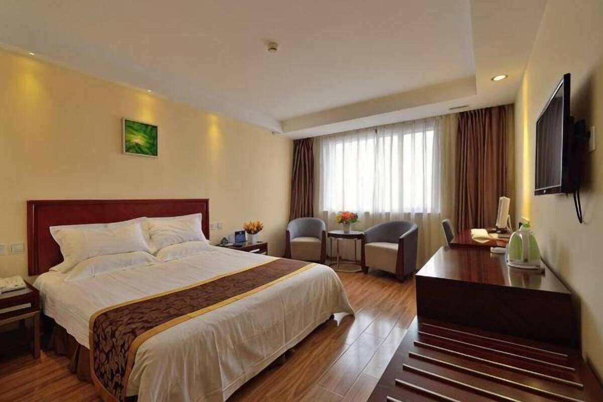 Habitación de hotel con una cama grande, un escritorio, una silla, un televisor y una ventana con cortinas.