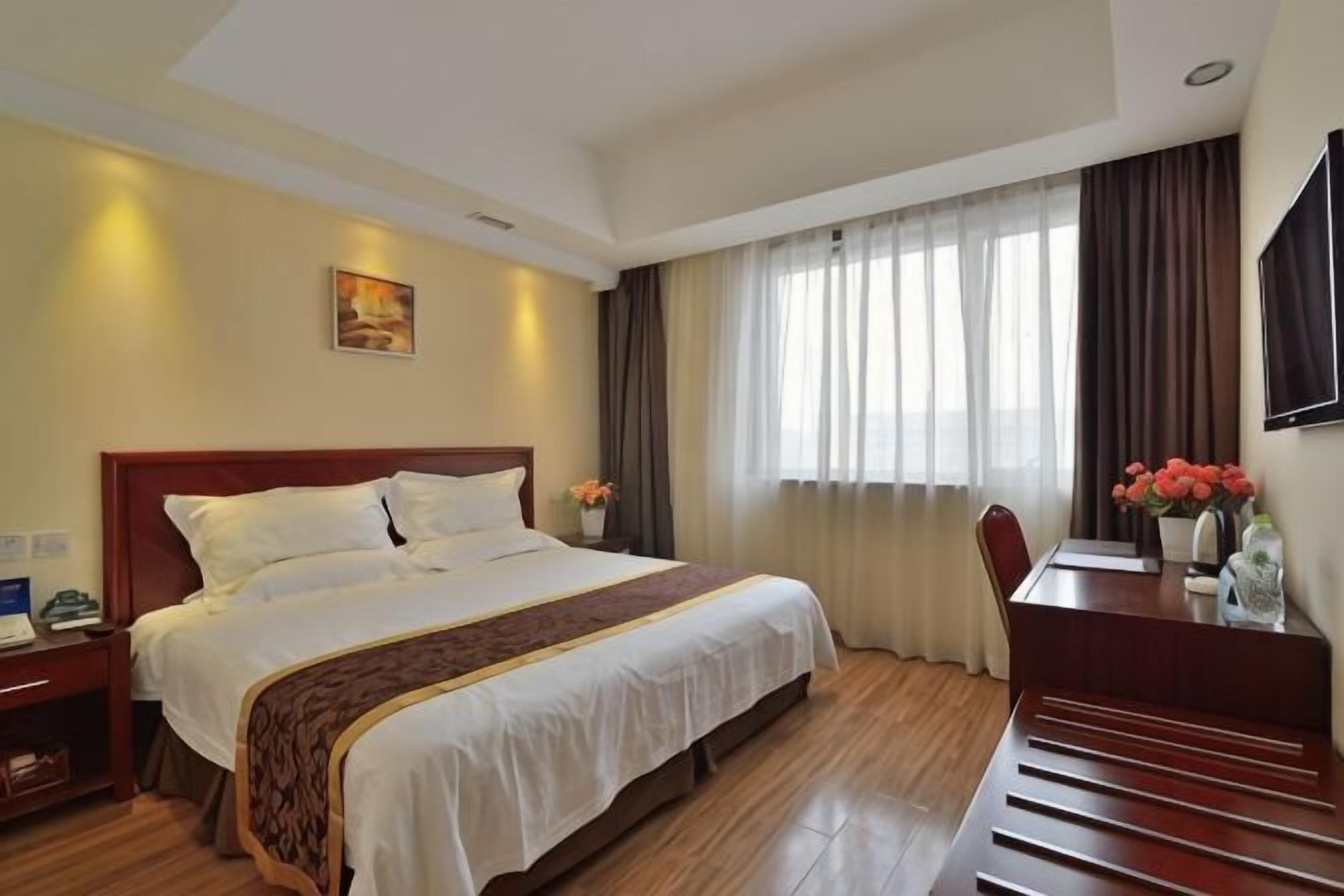 A hotel room with a large bed, a desk, a chair, a nightstand, and a TV on the wall.