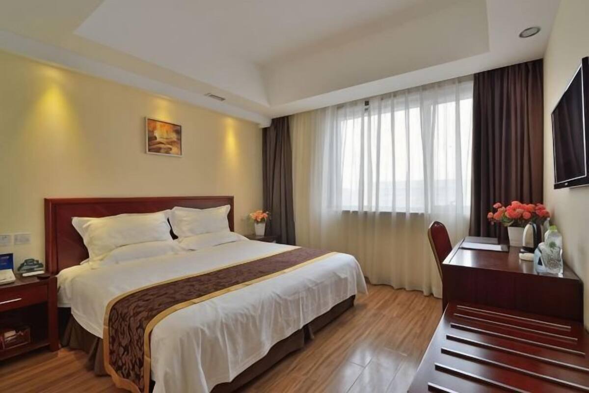 Habitación de hotel con una cama grande, un escritorio, una silla, una mesita de noche y un televisor en la pared.