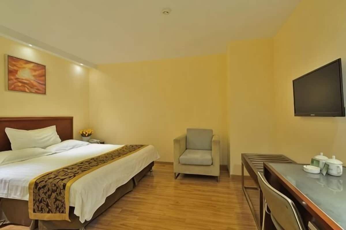 A hotel room with a bed, a chair, a desk, and a television.