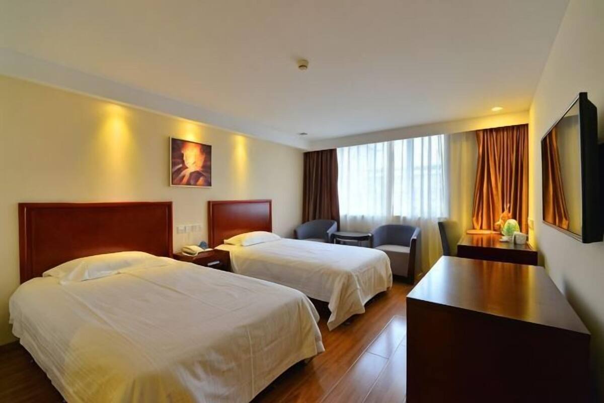 Habitación de hotel con dos camas, un escritorio, una silla, un televisor y una ventana con cortinas.
