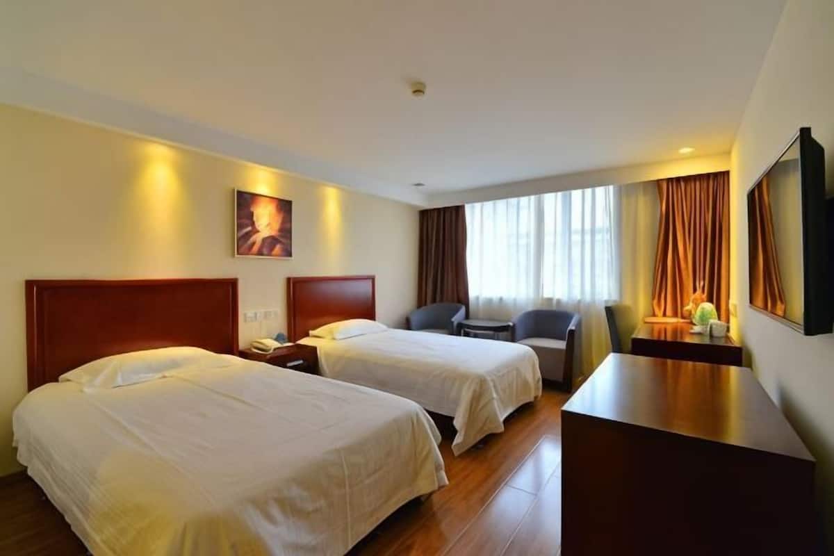 A hotel room with two beds, a desk, a chair, a TV, and a window with curtains.
