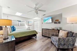A bedroom with a bed, a chair, a dresser, a television, and a ceiling fan. - Fanta-Sea on the Beach by Beachside Management - 53 Beach Rd (Siesta Key)