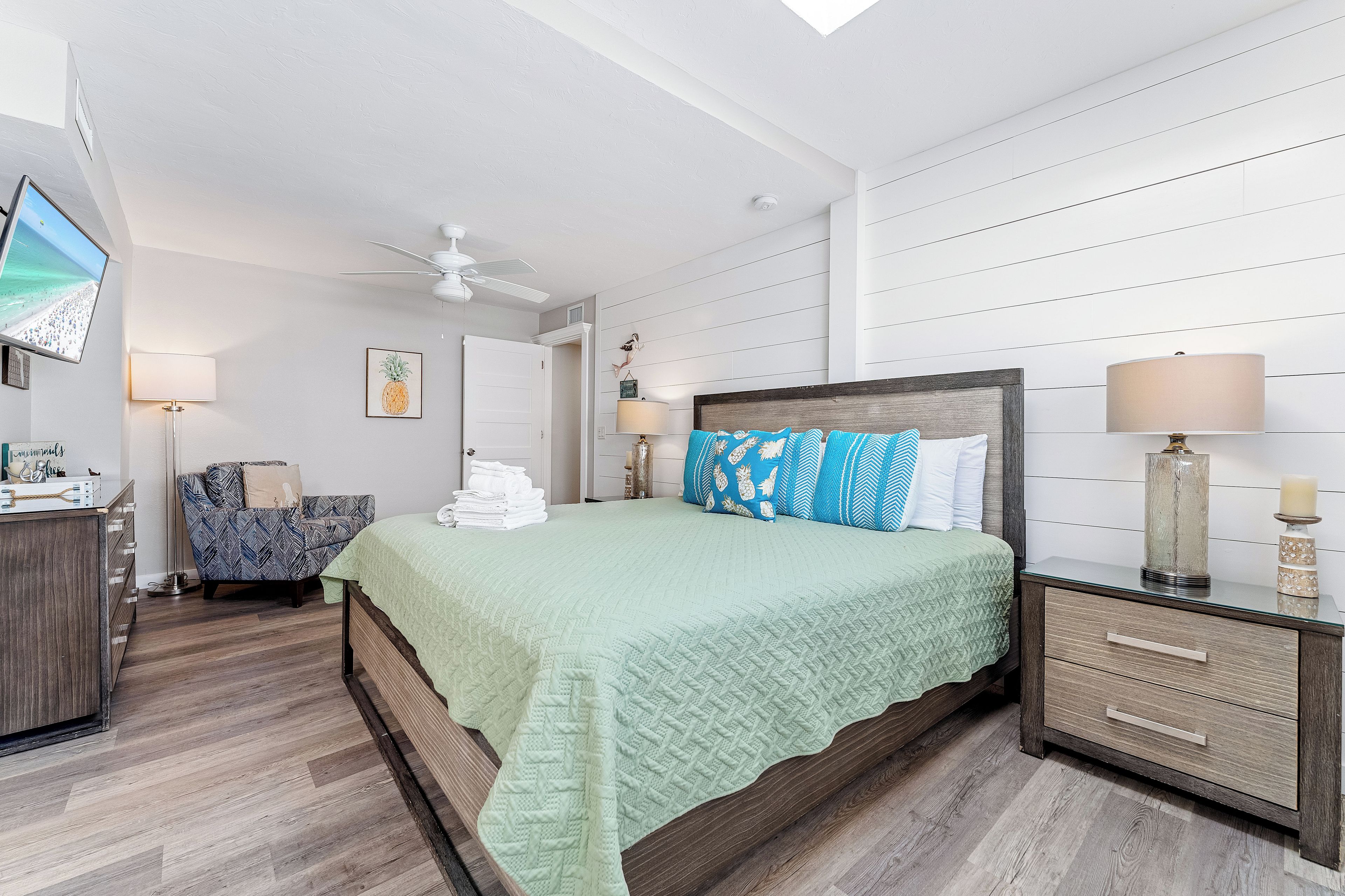 A hotel room with a bed, a television, a ceiling fan, and a view of the beach.
