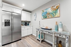 A modern kitchen with stainless steel appliances, white cabinetry, and a rustic wooden floor. - Fanta-Sea on the Beach by Beachside Management - 53 Beach Rd (Siesta Key)