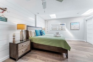 Un dormitorio con cama, mesita de noche, lámpara, decoración en la pared y ventana.