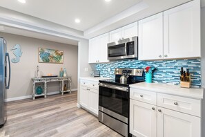 A modern kitchen with white cabinetry, stainless steel appliances, and a blue-tiled backsplash. - Fanta-Sea on the Beach by Beachside Management - 53 Beach Rd (Siesta Key)