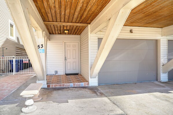 A covered entryway with a wooden ceiling, a white door, and a garage door. - Fanta-Sea on the Beach by Beachside Management - 53 Beach Rd (Siesta Key)