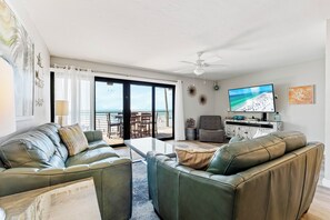 Una sala de estar con vista a la playa, un ventilador de techo y un televisor.